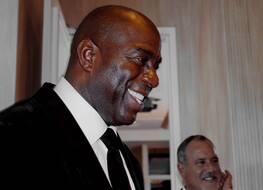 Magic Johnson in a suit smiling at something or someone
