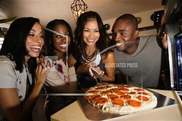 Four friends putting a pizza in the oven
