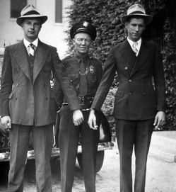 A 1927 photo of a police officer with two bank robbers in suits hand-cuffed to each other