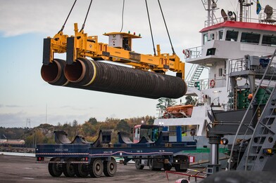 Two pipes the length of a living room being loaded onto a vessel