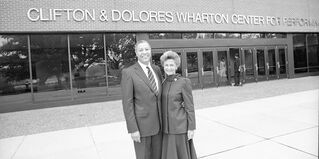 Clifton & Dolores Wharton smiling in front of the performing arts center named after them
