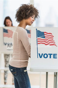 A woman of color with curly hair voting at a voting booth
