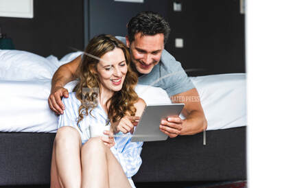A couple working on at a tablet together in bed