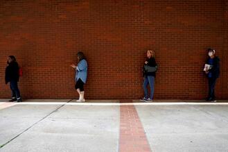 People waiting in line alongside a brick wall to file for unemployment benefits